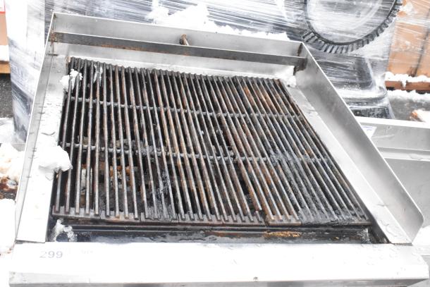 Commercial countertop charbroiler grill with equipment stand, metal grates, signs of wear, snow visible, tag number 299.