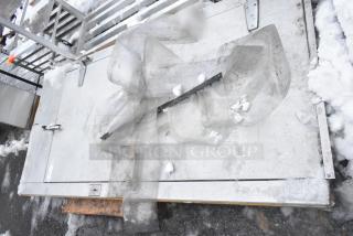 Walk-in door with frame, metal construction, visible wear, placed on snowy ground, includes hinges and handles.