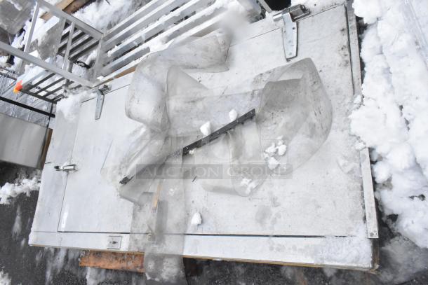 Walk-in door with frame, metal construction, visible hinges and latch. Snow-covered surface, fair used condition.