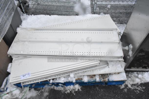 Pallet of white metal shelves with perforations, stacked in snowy outdoor setting. Label visible with "303."