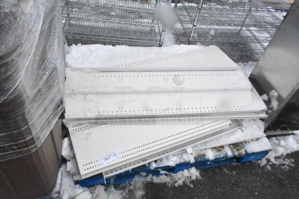 Pallet of white metal shelves, perforated design, stacked on a blue pallet, snow-covered, auction tag numbered 303.