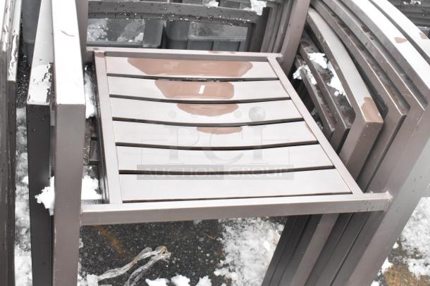 26 stackable brown outdoor armchairs with slatted seats, metal frames. Slight wear from outdoor use, visible snow and moisture.