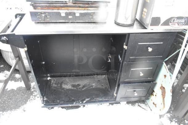 Black cart with three drawers on commercial casters, showing signs of wear. The interior is open, with some visible rust and scratches.