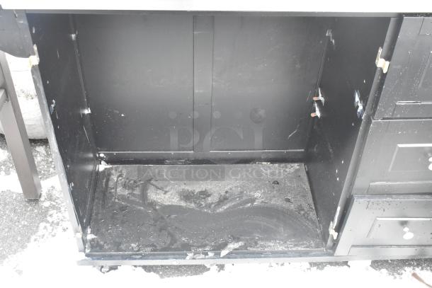 Black cart with three drawers, commercial casters; shows signs of wear, open compartment, sturdy construction.
