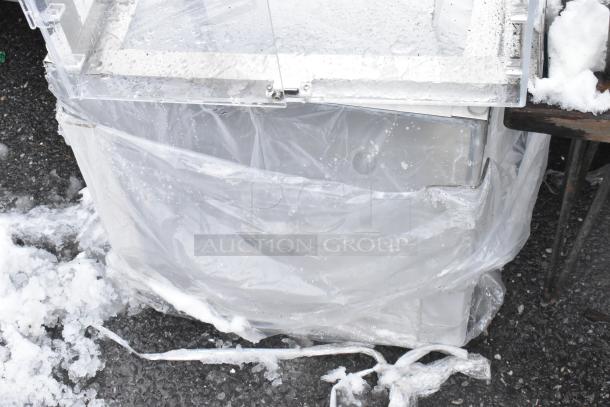 2 clear poly countertop cookie merchandisers, wrapped in plastic, pictured against a snowy ground.