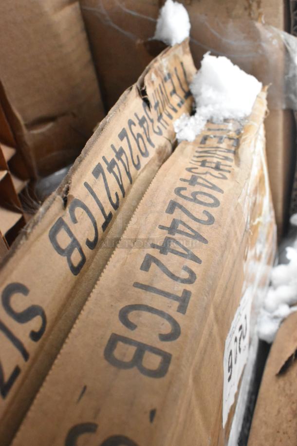 Cardboard boxes labeled with item codes, containing 8 new scratch-and-dent items: shelves and tabletop.