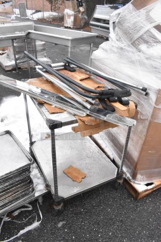 Stainless steel table with undershelf on commercial casters, featuring tray stands. Includes various contents, in used condition.