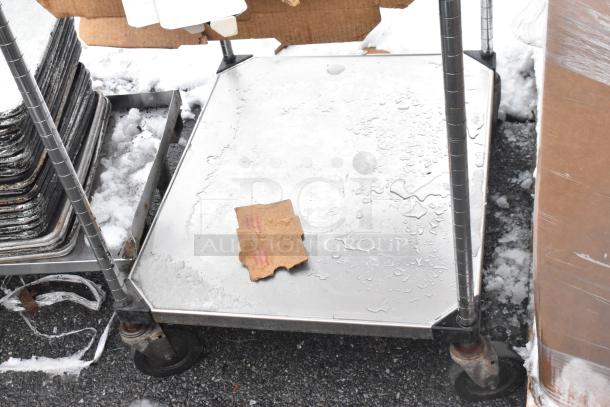 Stainless steel table on commercial casters with under shelf, includes tray stands. Visible wear, cardboard piece on surface.