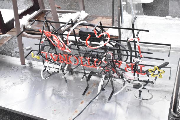 Shelf contents including a neon sign with a red and white design, and metal baking pans. Some signs of wear visible.