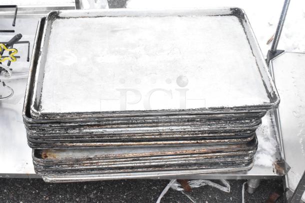 Stack of used metal baking pans on a shelf, showing signs of wear and rust. Neon sign partially visible in the background.
