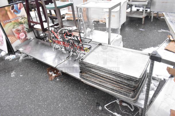 Shelf with contents including a neon sign and a stack of metal baking pans on a metal surface, outdoor setting.