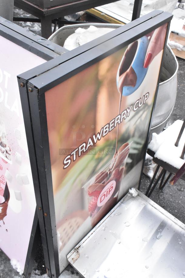 Two A-frame sidewalk signs, featuring "Strawberry Cup" with chocolate dip imagery. Good condition. Snow-covered base.