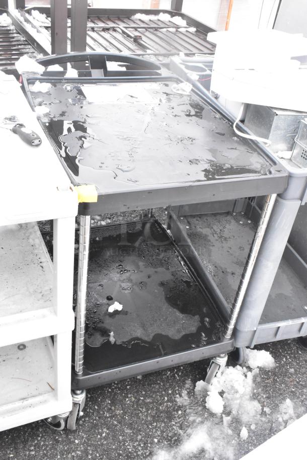 Three poly 2-tier carts with commercial casters, black and white, outdoor setting, wet surfaces, robust build.