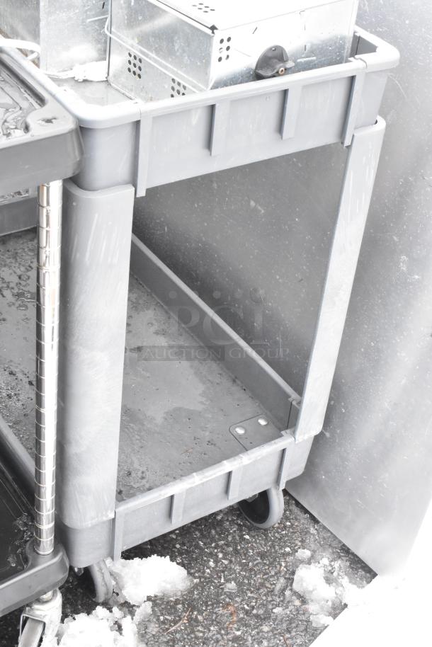 Gray 2-tier poly cart on commercial casters. Visible shelves, sturdy construction, used condition, ideal for heavy-duty use.