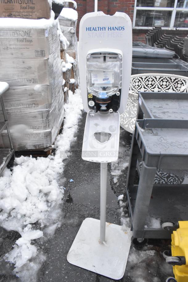 Hand sanitizer dispenser stand labeled "Healthy Hands Start Here," with yellow mop bucket nearby; both in fair condition.