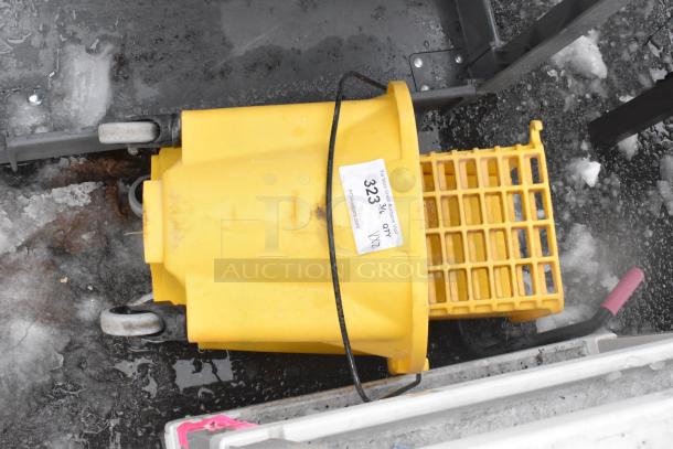 Yellow mop bucket with wheels and grating, labeled "323 3% OXY XYZ," on wet pavement, showing signs of use.