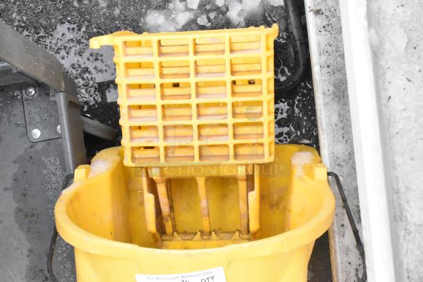 Yellow mop bucket with wringer, used condition, on a wet surface. Includes caution sign. Auction item, bid multiplies by two.