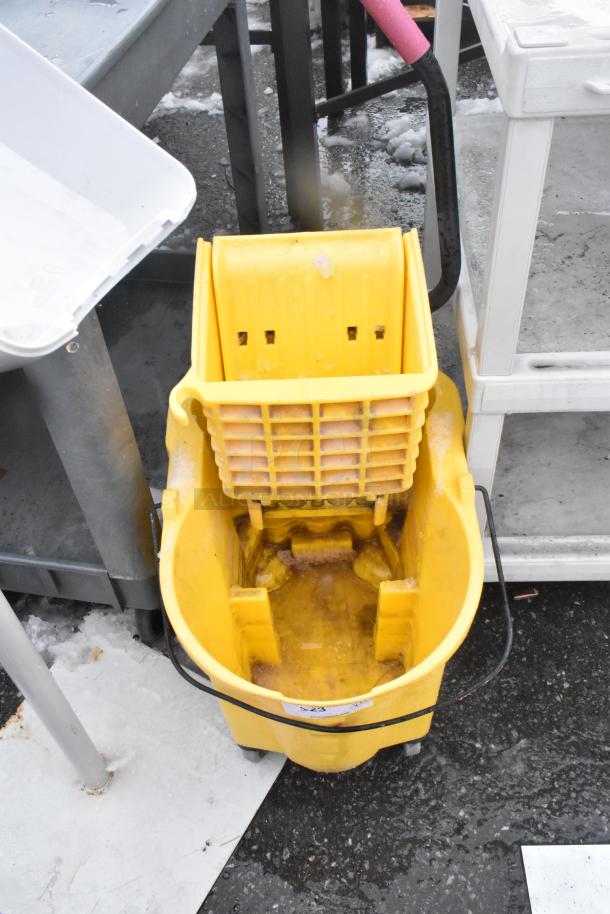 Yellow mop bucket with wringer, used condition, visible dirt and wear. Includes caution label. Auction for two items.