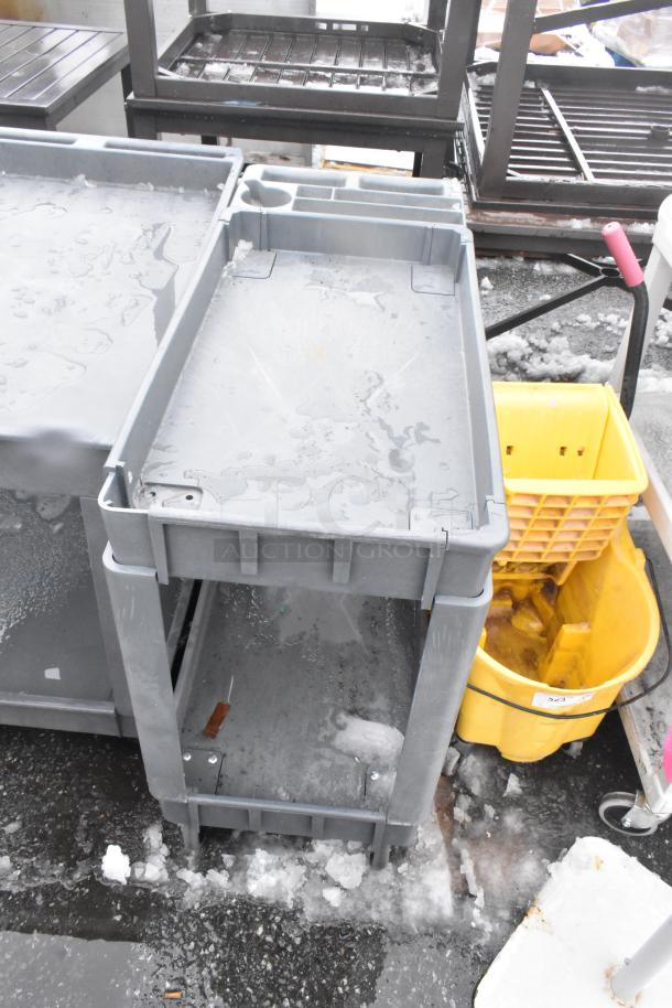 Gray two-tier poly cart with commercial casters, slightly worn, suitable for storage and transport.