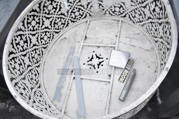 Ornate white metal bin with decorative cutout design, used condition. Contains metallic objects and a label marked "REST ROOM".