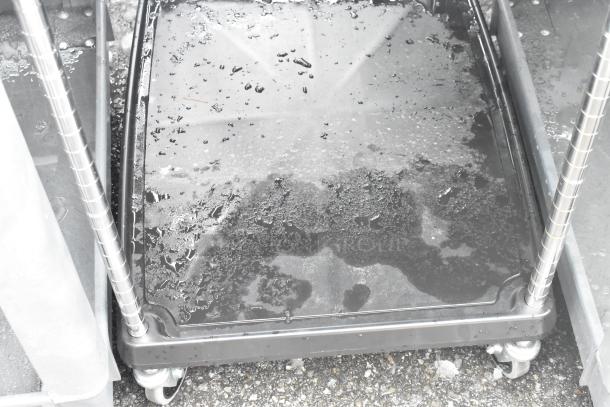 Black 2-tier cart on commercial casters with wire racks, shows wet surface. Ideal for storage or transport, sturdy condition.