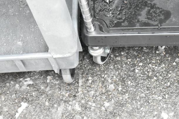 Black 2-tier cart with commercial casters, includes wire racks, visible detail of wheels, wet surface condition.