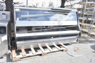 Commercial floor-style warming display case merchandiser, glass front, metal frame, resting on a pallet, visible controls.