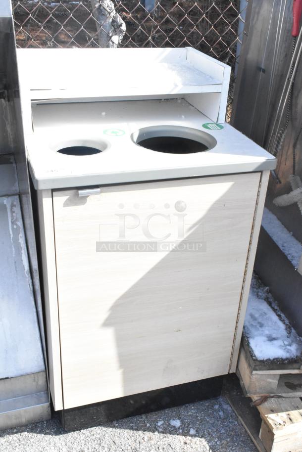 Wooden trash can shell with dual openings, recycling symbols, and a shelf. Appears in used condition outdoors.