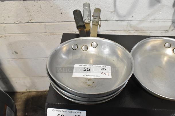 Stack of 11 metal skillets with riveted handles, showing moderate wear. Auction label indicates quantity and online auction site.