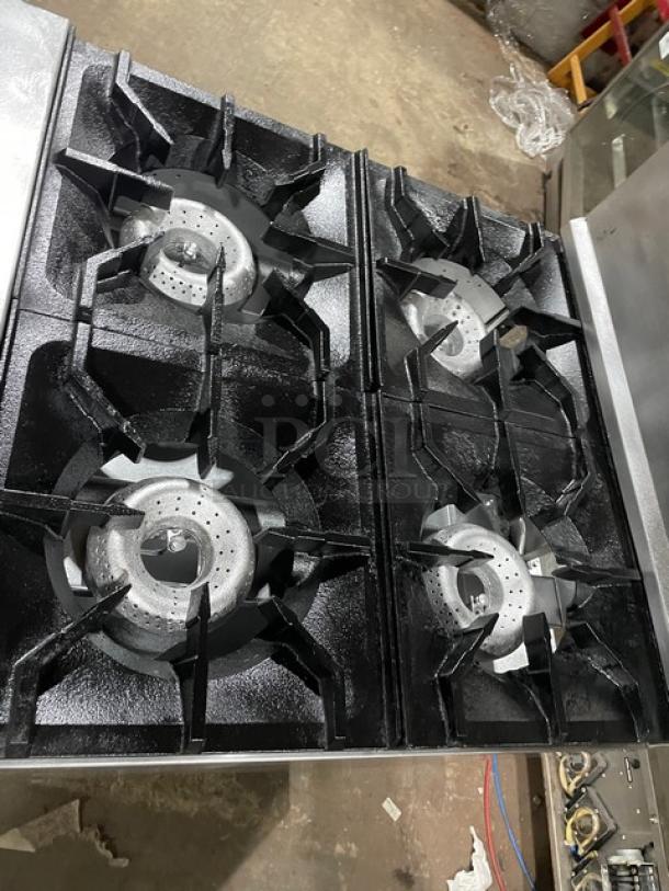 American Range stainless steel gas-powered 4-burner range/oven combo, featuring a backsplash, overhead salamander shelf, and wired oven rack, mounted on legs.