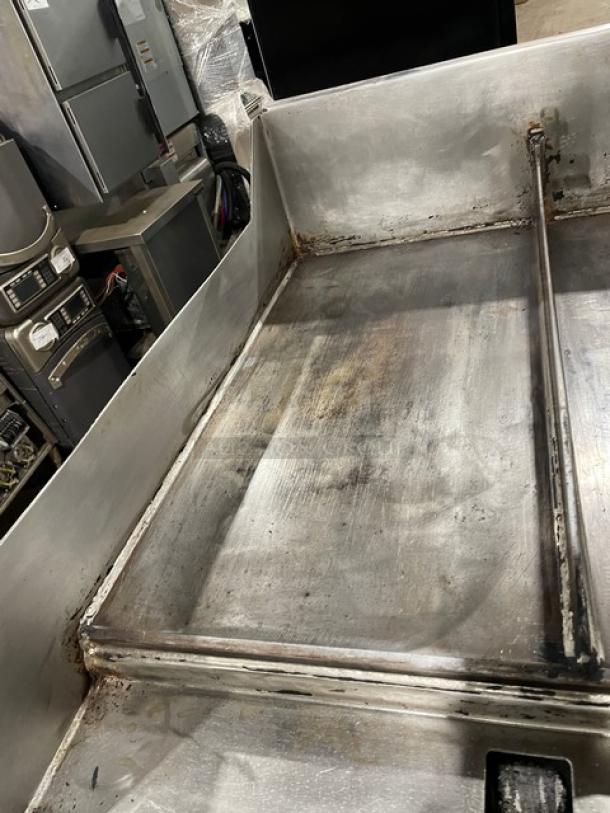 WoodStone stainless steel gas countertop plancha griddle, split-top, with back and side splash, shows wear, on legs.