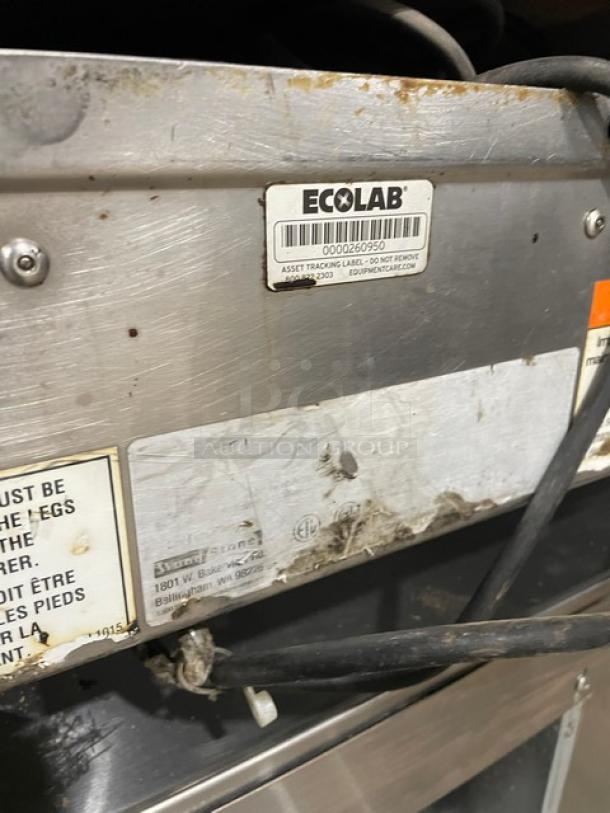 WoodStone commercial stainless steel gas-powered countertop plancha griddle. Features split-top style, with back and side splash, and sturdy legs. Visible labels include "Ecolab" asset tag.