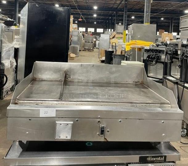 WoodStone commercial stainless steel gas-powered plancha griddle, split-top style, with back and side splash, on legs, countertop model.