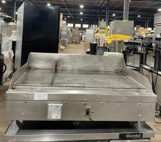 WoodStone commercial stainless steel gas-powered plancha griddle, split-top style, with back and side splash, on legs, countertop model.