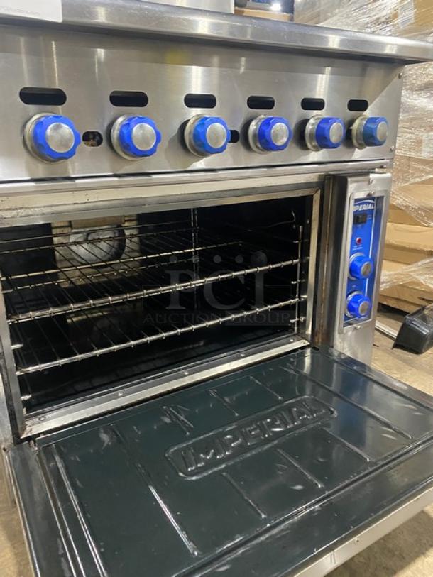 Imperial stainless steel gas char broiler range/oven combo with backsplash, blue controls, and wired oven rack on casters.