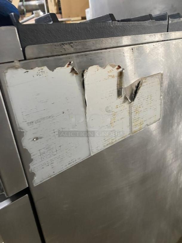 CookRite stainless steel 4-burner gas range/oven with back splash, overhead salamander shelf, and casters. Worn labels visible.