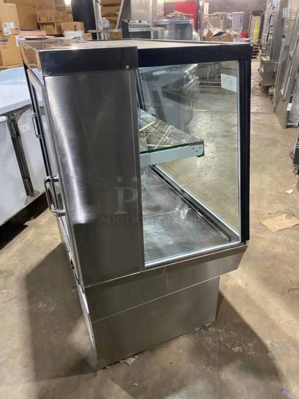 Commercial stainless steel slanted glass refrigerated bakery display case, multi-tier, rear sliding glass doors, on legs.