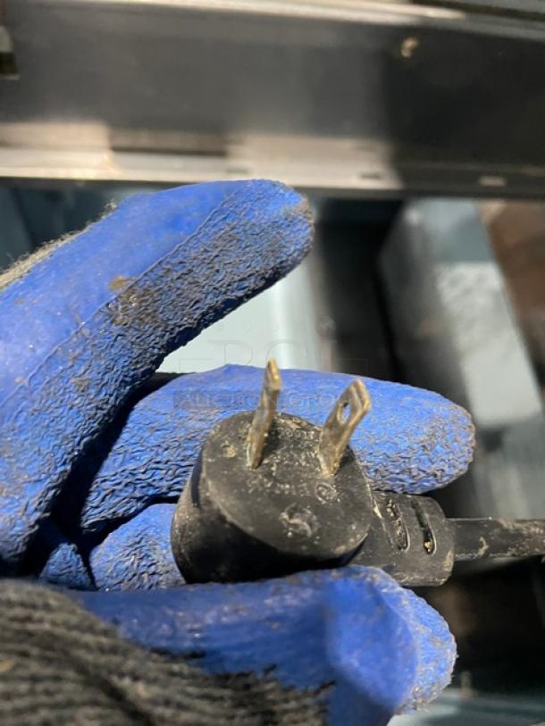 Close-up of a black electrical plug held by a blue-gloved hand, part of Delfield prep table model 4432N12M.