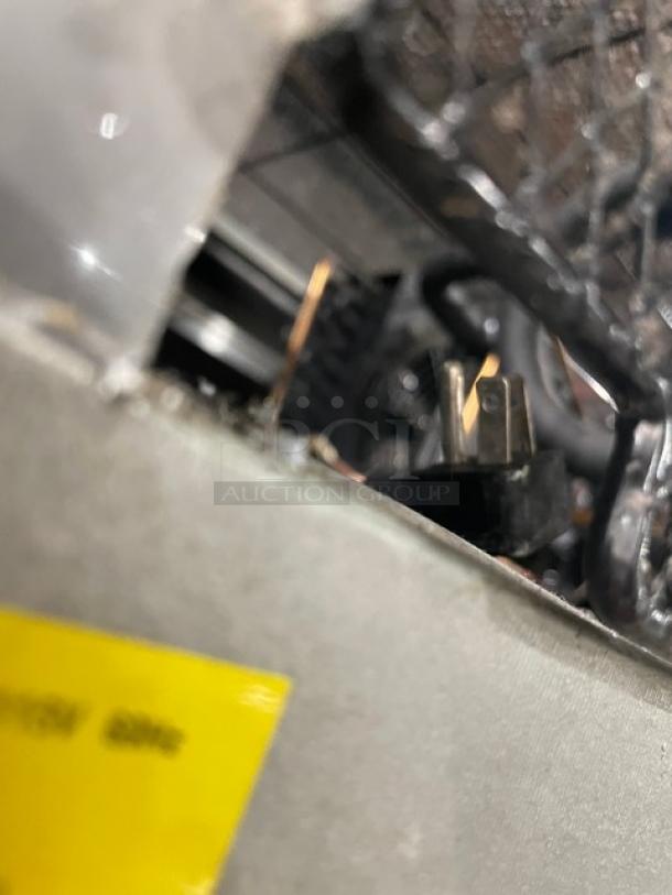 Blurred image showing the edge of a Maxx Cold reach-in freezer with visible electrical plug and wiring. Visibility of item details is limited.