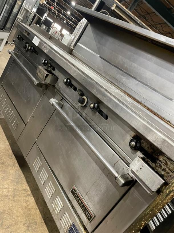 Garland H289RC72GTH stainless steel natural gas flat griddle range/double oven combo with back & side splash, overhead salamander shelf, on casters.
