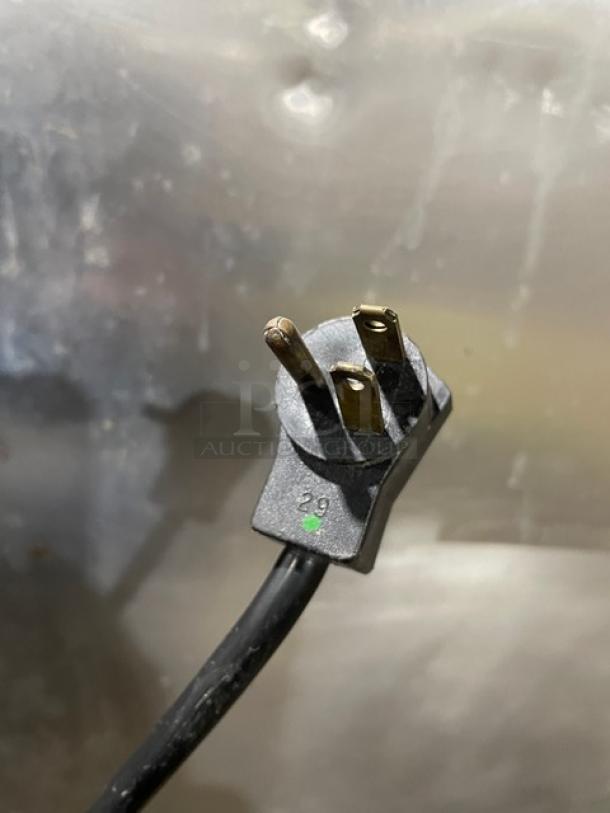 Power plug for Delfield 6000-XL Series commercial freezer, black cord, metal prongs, against stainless steel background.