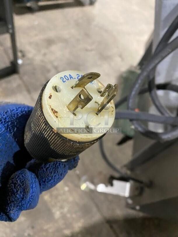 A 20A, 250V electric plug in a blue-gloved hand, connected to the Moline commercial dough sheeter/molder.