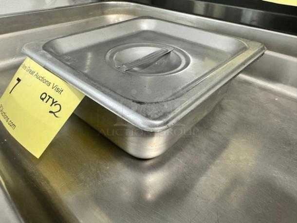 Lot of 2 stainless steel food pans with lids, slight wear, stacked on metal surface with marked auction tags.