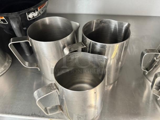 Lot of 3 stainless steel 20oz milk frothing pitchers. Used condition, showing minor wear. Clean lines, sturdy handles.