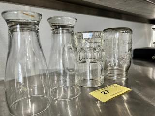 Lot of 4 miscellaneous glass containers on metallic shelf; includes carafes and jars, varying shapes, in good condition.