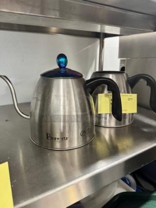 Two Brewista pour-over gooseneck kettles on a shelf, one missing a lid. Both have ergonomic handles and stainless steel bodies.