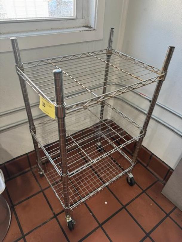 Chrome-finish utility cart with three wire shelves, caster wheels, and a labeled tag. In good condition.