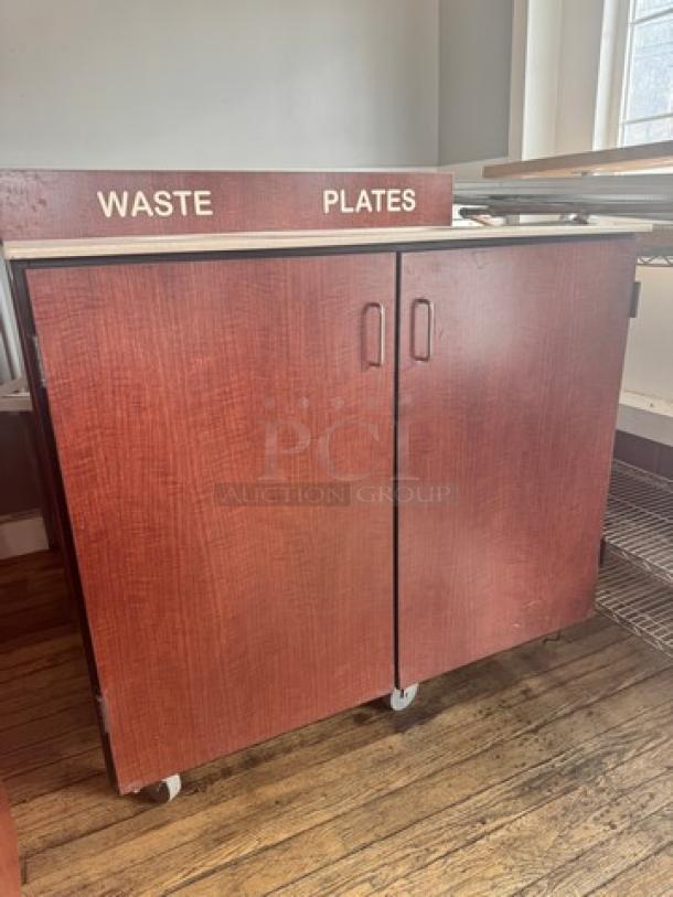 Red wooden waste receptacle with "Waste" and "Plates" labels, double doors, and caster wheels. Suitable for restaurant use.