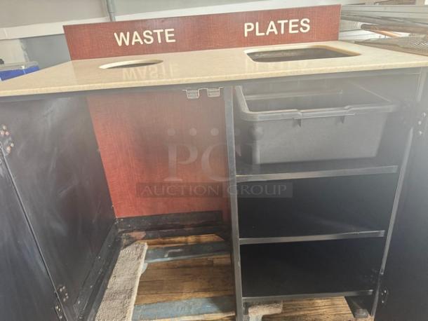 Commercial waste receptacle with dual sections labeled "Waste" and "Plates." Features a wooden panel and storage shelf.