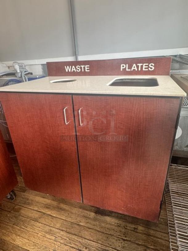 Wooden waste receptacle with dual openings labeled "Waste" and "Plates." Features stainless steel handles and countertop.